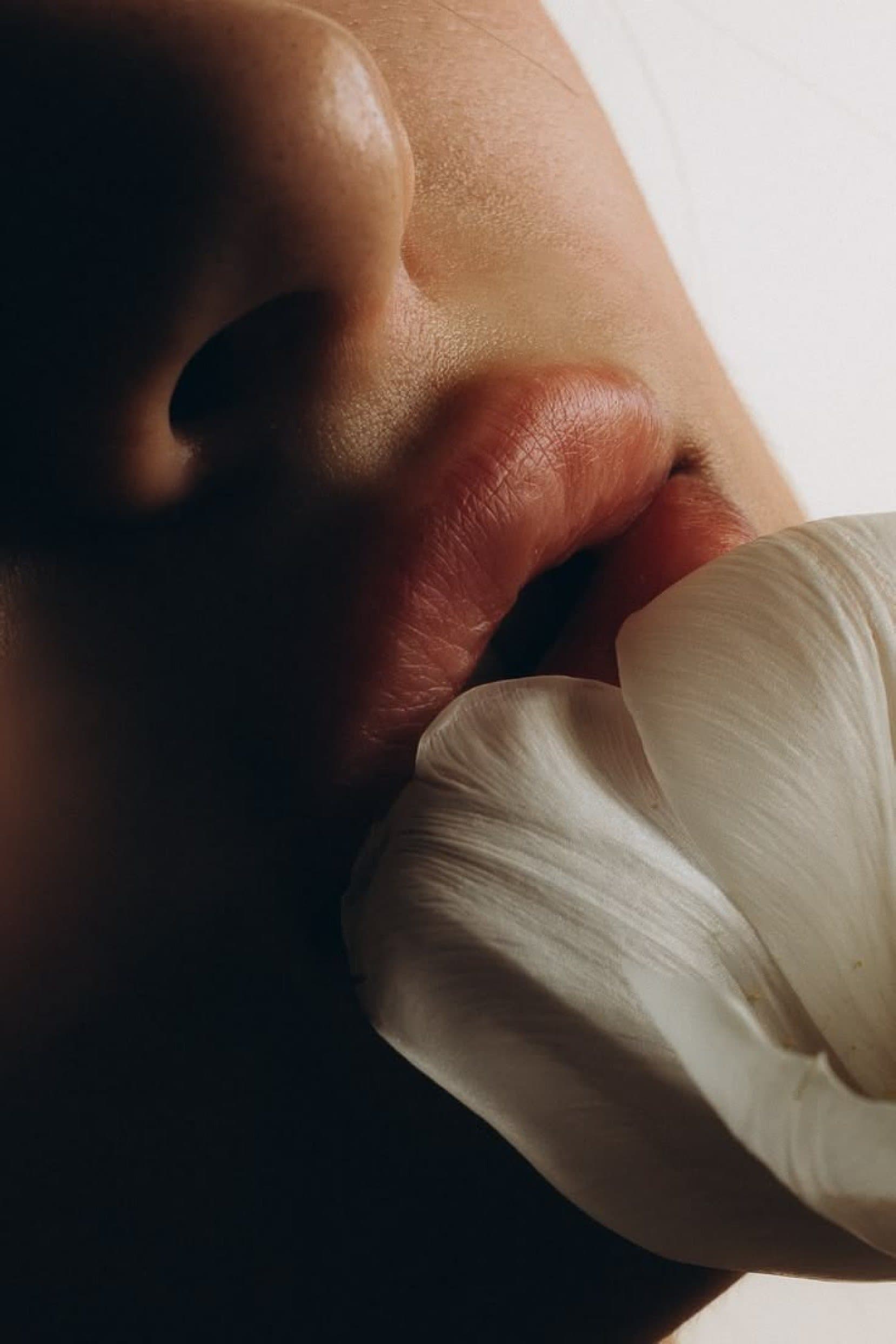 Close-up of lips resting against a pale petal in warm, low light